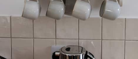 A kitchen with a white cabinet holding plates and glasses, a kettle, and a toaster on the counter.