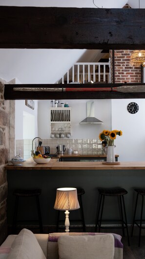A kitchen with a wooden counter, a hanging light fixture, and a clock on the wall.