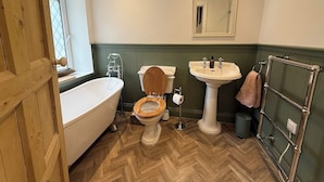 A bathroom with a wooden door, a white bathtub, a wooden toilet, a pedestal sink, and a towel rack. - Peaceful Granite Cottage: Walk to St Brelade's Bay Beach and St Aubin Harbour (St Brelade)