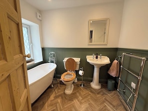 Un bagno con porta in legno, una vasca da bagno bianca, un water in legno, un lavabo su piedistallo e un portasciugamani.