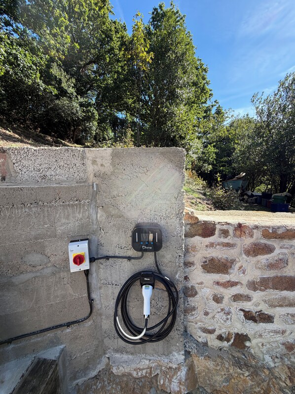 An outdoor electrical charging station mounted on a stone wall with a cable connected to it.