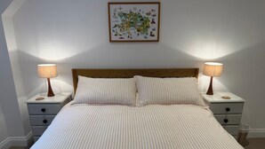 A neatly made bed with striped bedding, two bedside tables with lamps, and a wall-mounted picture. - Peaceful Granite Cottage: Walk to St Brelade's Bay Beach and St Aubin Harbour (St Brelade)