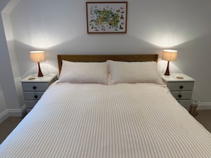 Un letto rifatto con biancheria a righe, due comodini con lampade e un quadro appeso al muro.