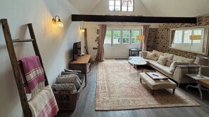 A cozy living room with a high ceiling, a stone wall, a wooden ladder, a sofa set, a coffee table, and a rug. - Peaceful Granite Cottage: Walk to St Brelade's Bay Beach and St Aubin Harbour (St Brelade)