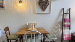A dining area with a wooden table, two chairs, a wall-mounted light, and a heart-shaped decoration.