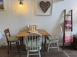 A dining area with a wooden table, two chairs, a wall-mounted light, and a heart-shaped decoration.