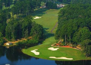 Un campo de golf con búnkeres de arena, una masa de agua y árboles densos.