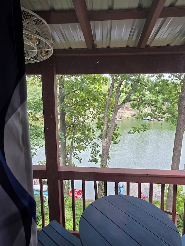 Un espacio exterior techado con una mesa y sillas, con vista a un cuerpo de agua y árboles.