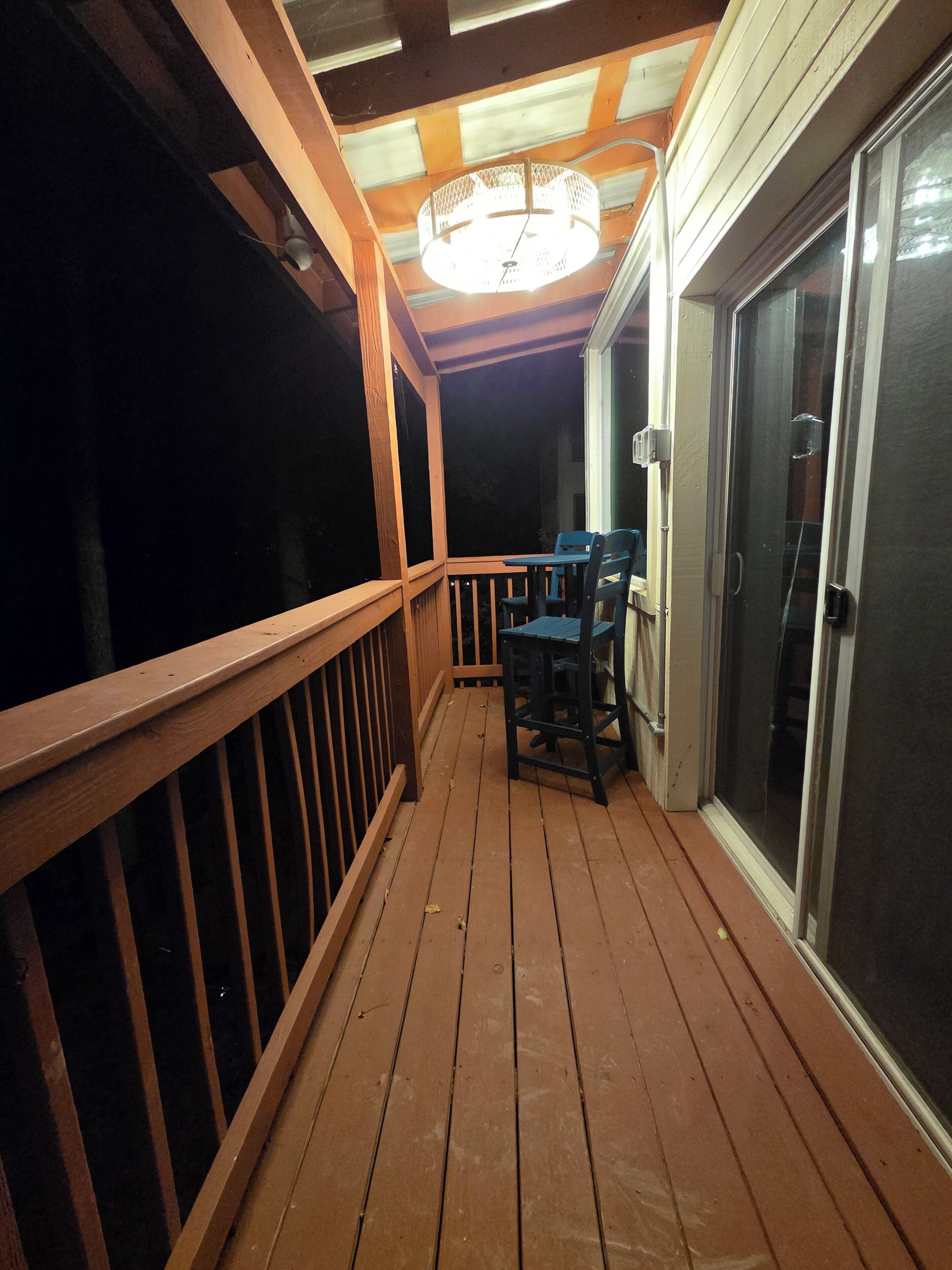 A wooden deck with a railing, a table, and chairs, leading to a sliding glass door.