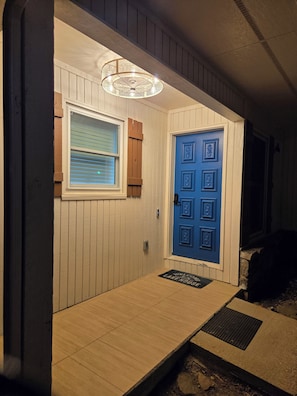 A wooden door with a blue panel, a window with blinds, and a light fixture above the door.