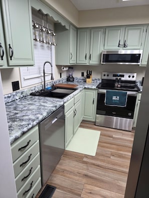 Una cocina con gabinetes verde claro, estufa de acero inoxidable y encimera de granito.