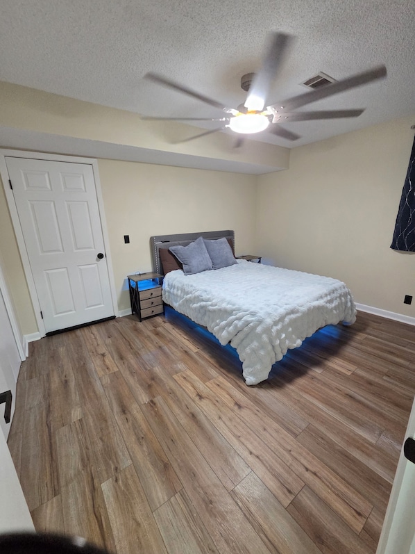 A bedroom with a bed, a ceiling fan, a door, and a nightstand.