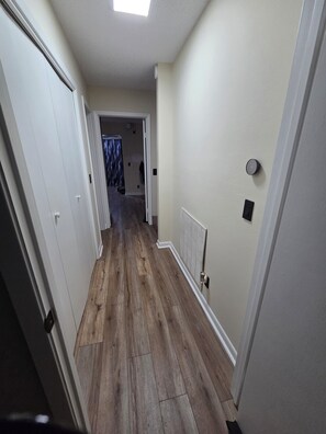 Un pasillo con piso de madera, paredes blancas y un radiador.
