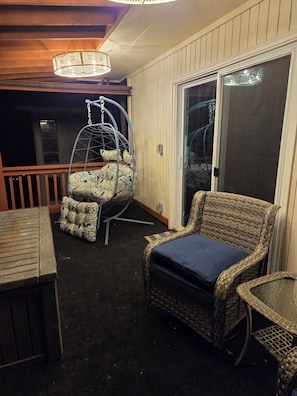 Un patio con una silla de mimbre, un sillón colgante con cojines estampados y una mesa de madera.