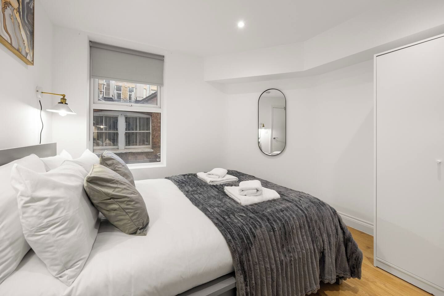 A bedroom with a bed, a window, a mirror, and a wardrobe.