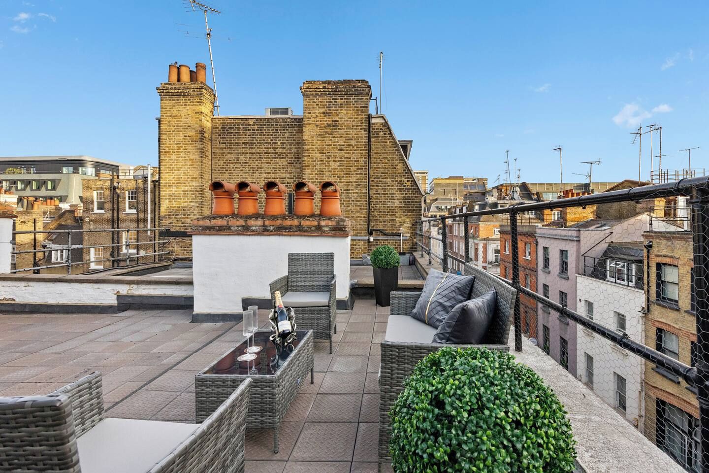 A rooftop terrace with a brick chimney, outdoor seating, and a view of the cityscape.