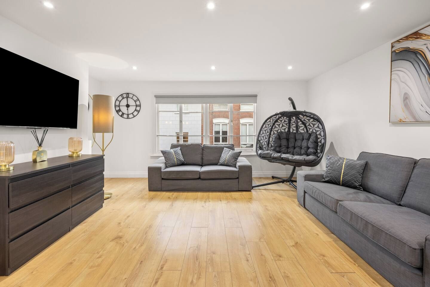 A modern living room with a grey sofa, a hanging chair, a flat-screen TV, and a large window.