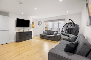 Ein modernes Wohnzimmer mit Fernseher, einer Couch, einem Sessel und einer Wanduhr.