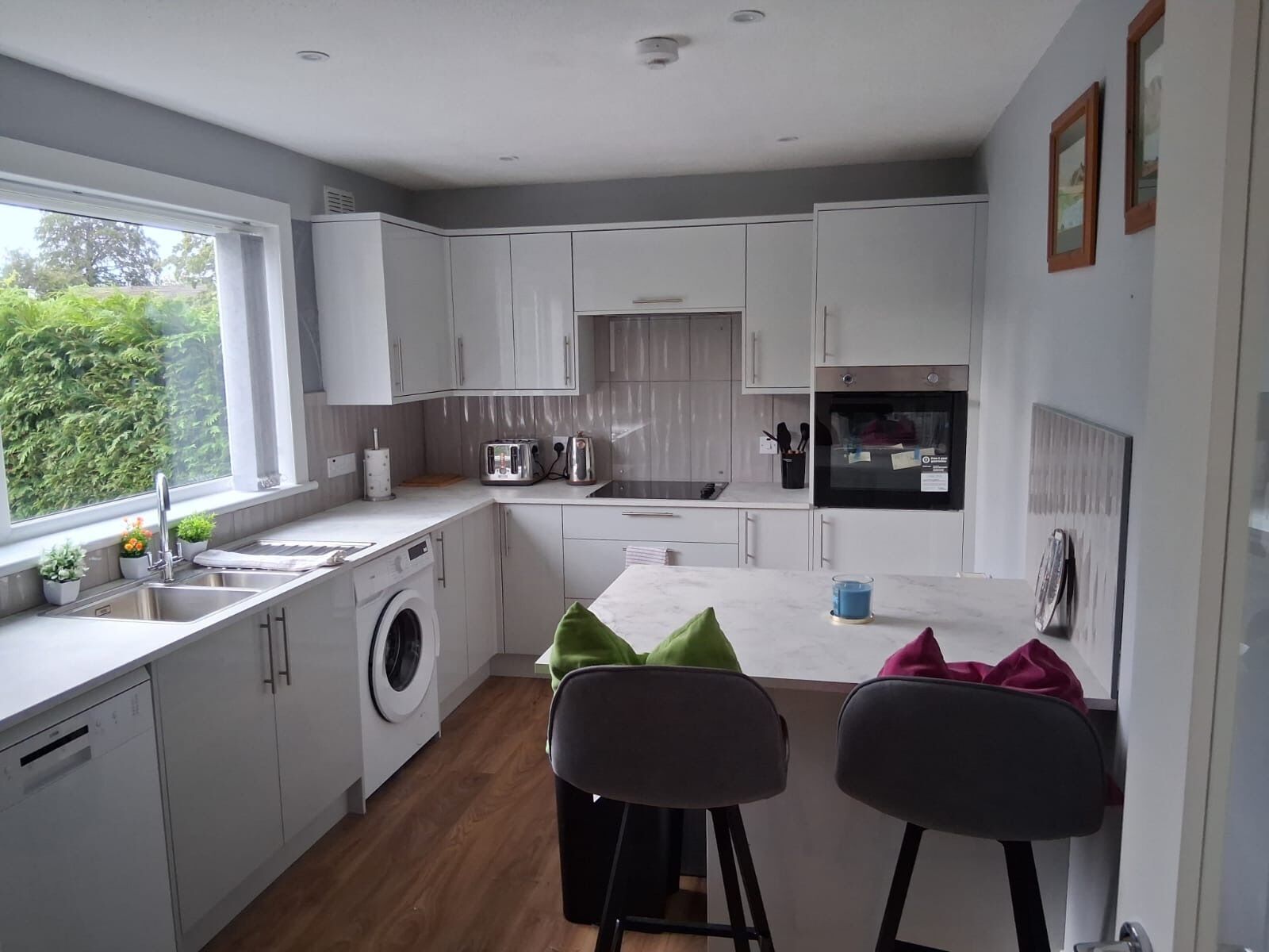 A modern kitchen with white cabinets, a washing machine, and a dining area with two chairs.
