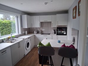 A modern kitchen with white cabinets, a washing machine, and a dining area with two chairs. - Cosy and bright spacious 3 bedroom house in a quiet cul de sac area in Culloden (Culloden)