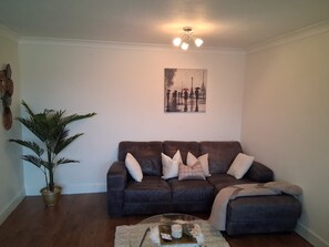 A living room with a brown leather sofa, a potted plant, a coffee table with a candle, and a painting on the wall. - Cosy and bright spacious 3 bedroom house in a quiet cul de sac area in Culloden (Culloden)