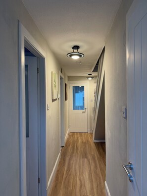 A hallway with a wooden floor, white walls, and a door at the end. - Cosy and bright spacious 3 bedroom house in a quiet cul de sac area in Culloden (Culloden)