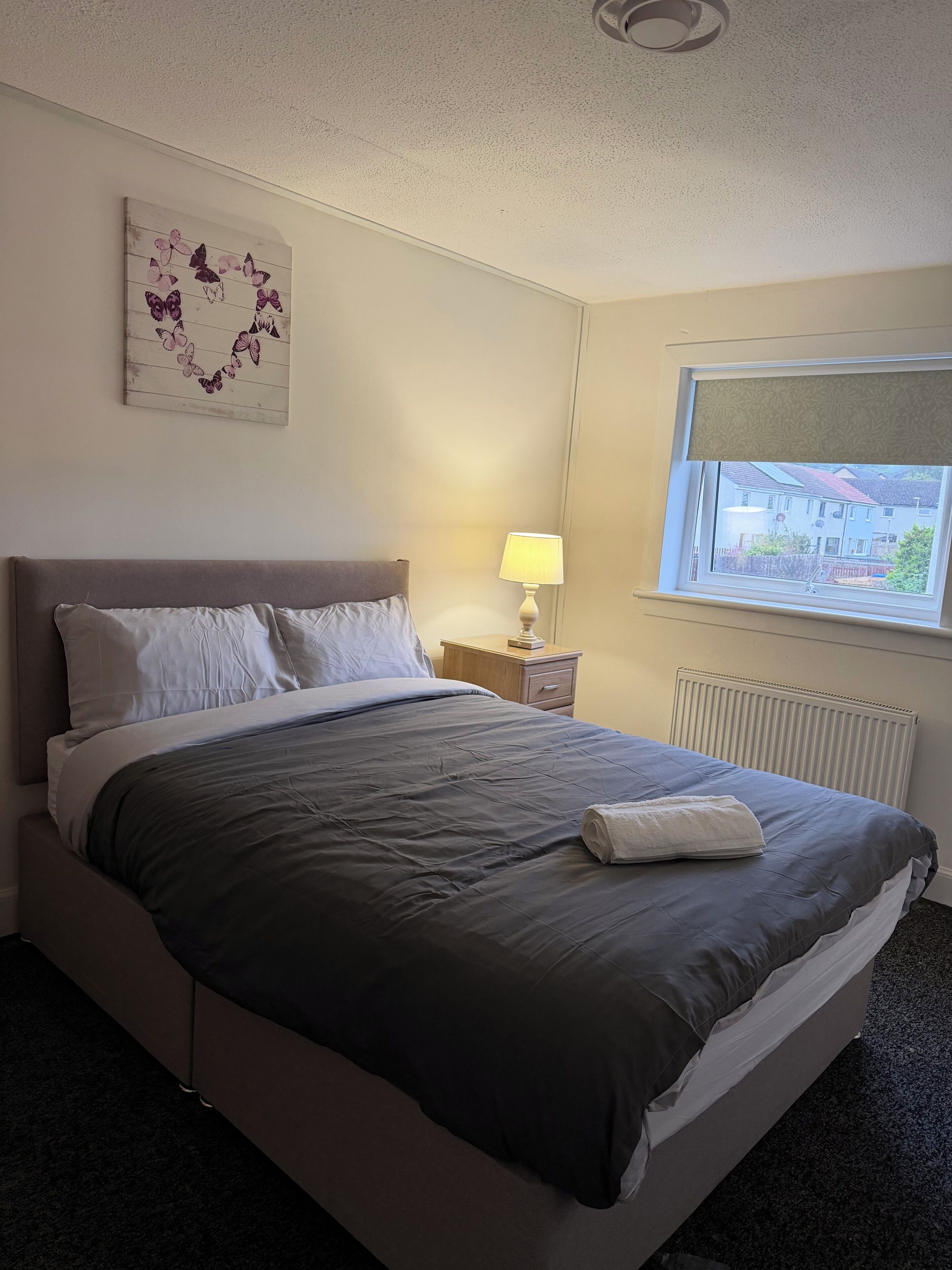 Ein Hotelzimmer mit einem Bett, einem Nachttisch mit Lampe, einem Fenster mit Blick und einer Wanddekoration.