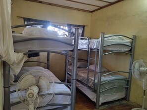 Een slaapkamer met een stapelbed, een ventilator en een raam met gordijn.