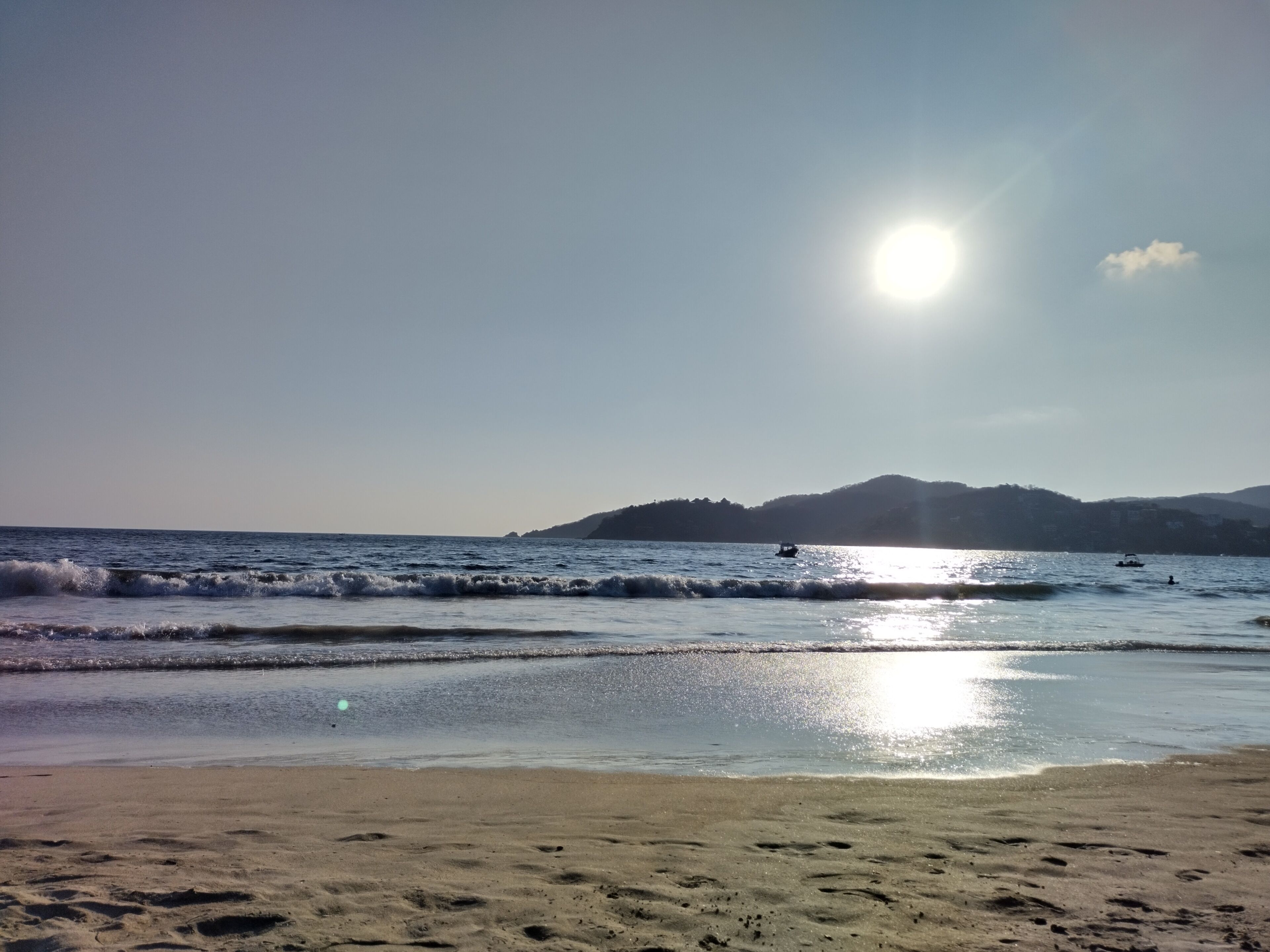 A beach with waves, a boat, and a distant mountain.