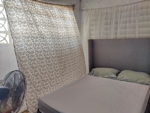 Een kamer met een bed, een ventilator en gordijnen met een patroon.