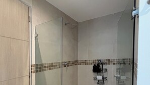 Eine Duschkabine mit Glas, ein gefliester Boden und eine kleine Ablage für Pflegeprodukte.