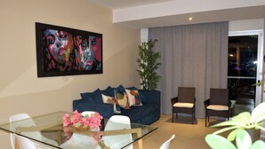 Ein modernes Wohnzimmer mit einem Glastisch, weißen Stühlen, einem blauen Sofa und einem großen abstrakten Gemälde an der Wand.