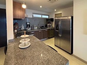 A modern kitchen with granite countertops, stainless steel appliances, and wooden cabinets. - Private Terrace with Views of the Ocean and the Tajamar Lagoon (Cancún)