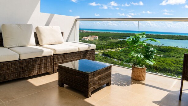 Ein Balkon mit einer Rattan-Couch, einem Glastisch und einem Blumentopf.