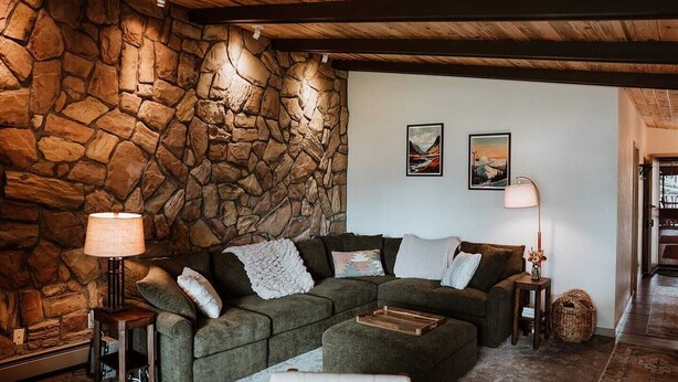 Ein gemütliches Wohnzimmer mit Steinwand, einem Ecksofa und zwei Wandleuchten.