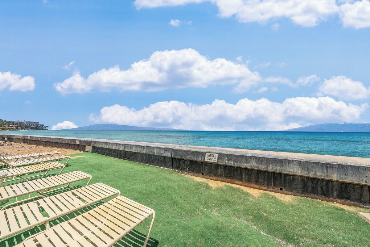 A beachside view with lounge chairs, a concrete barrier, and a clear sky.
