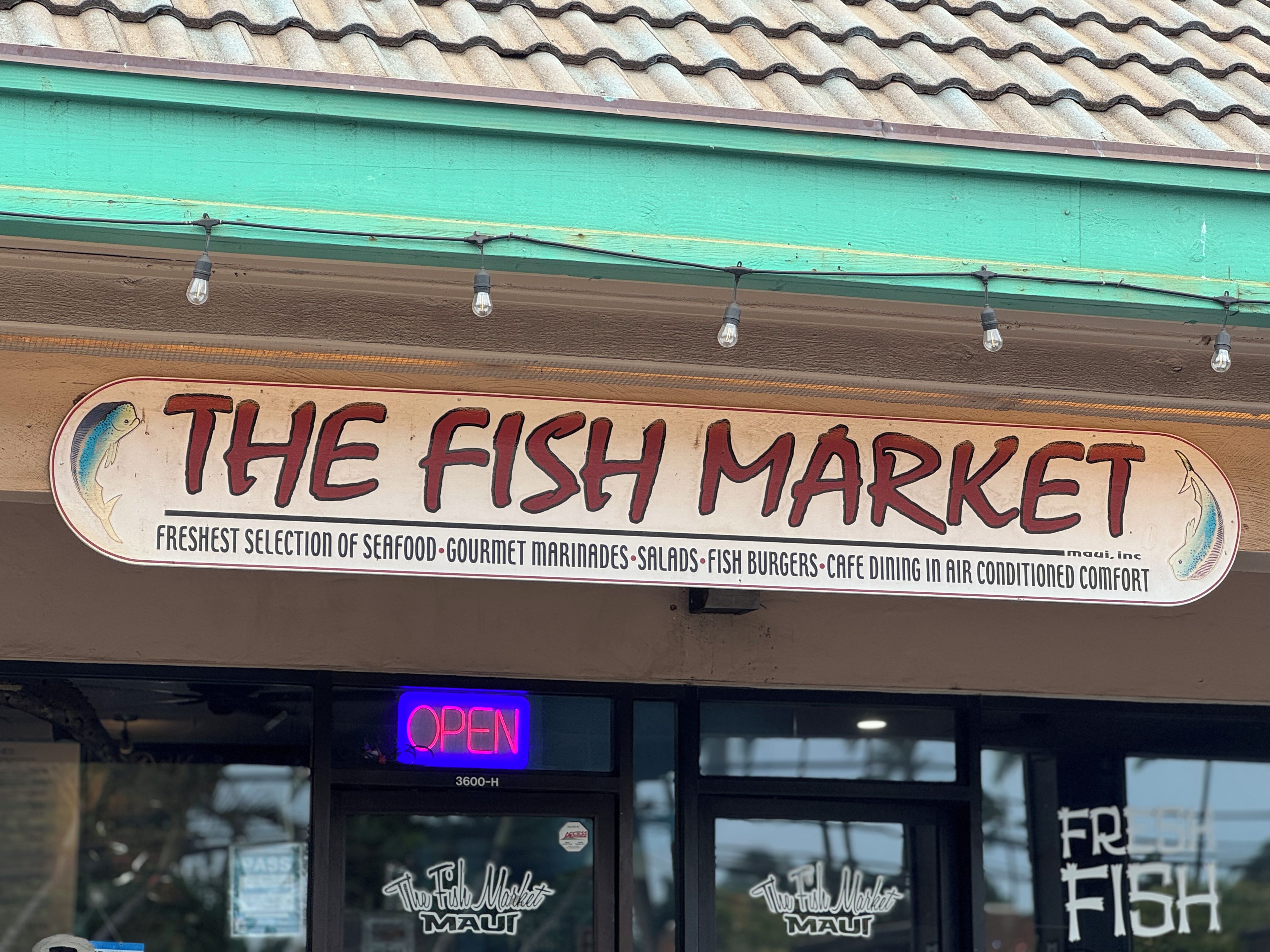 Ein Ladenlokal mit einem Schild, das "The Fish Market" zeigt, bietet Meeresfrüchte, Marinaden, Salate, Fischburger und die Möglichkeit, im Café zu essen.