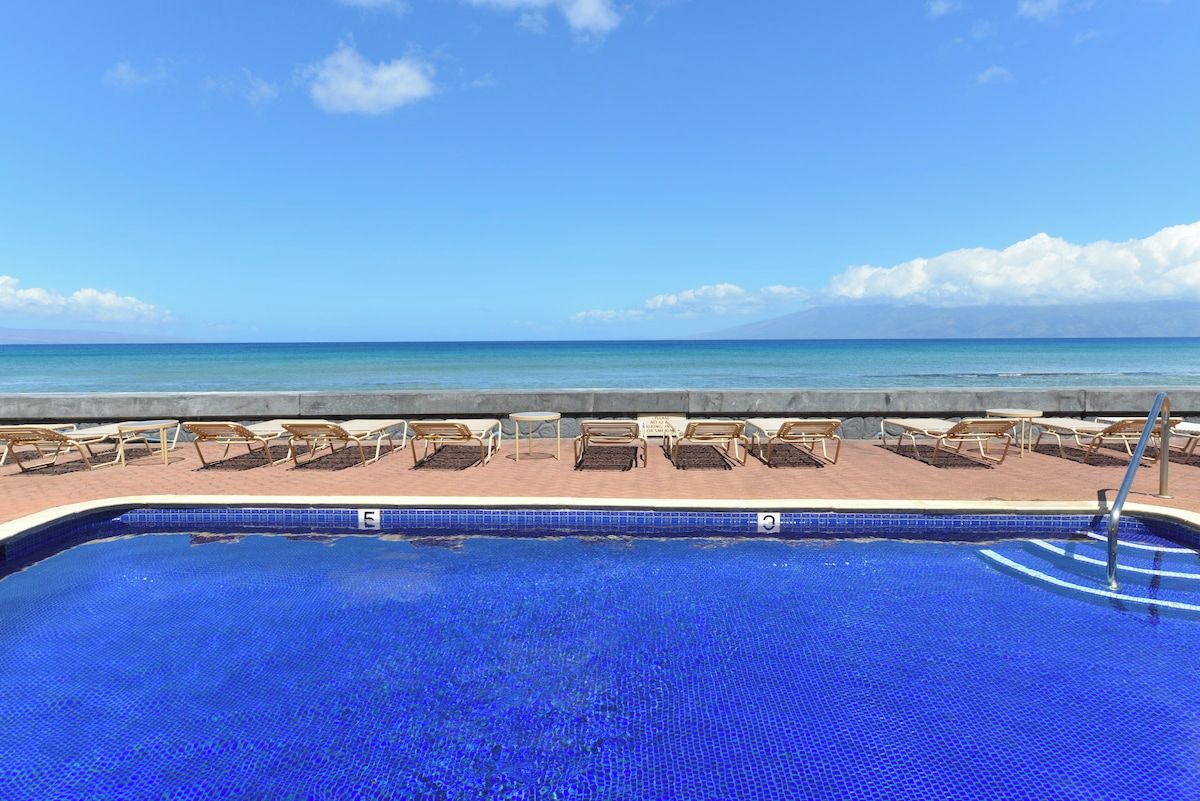A swimming pool with lounge chairs facing the ocean.