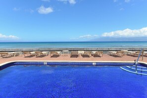 A swimming pool with lounge chairs facing the ocean.