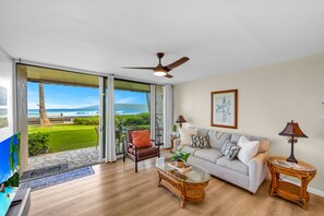 A spacious living room with a large sliding glass door leading to a balcony with a view of the ocean.