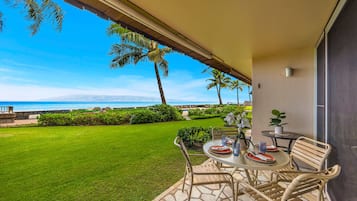 A patio with a table and chairs, a view of the ocean, and a well-maintained lawn.