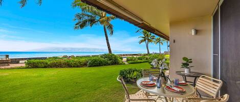 A patio with a table and chairs, a view of the ocean, and a well-maintained lawn.