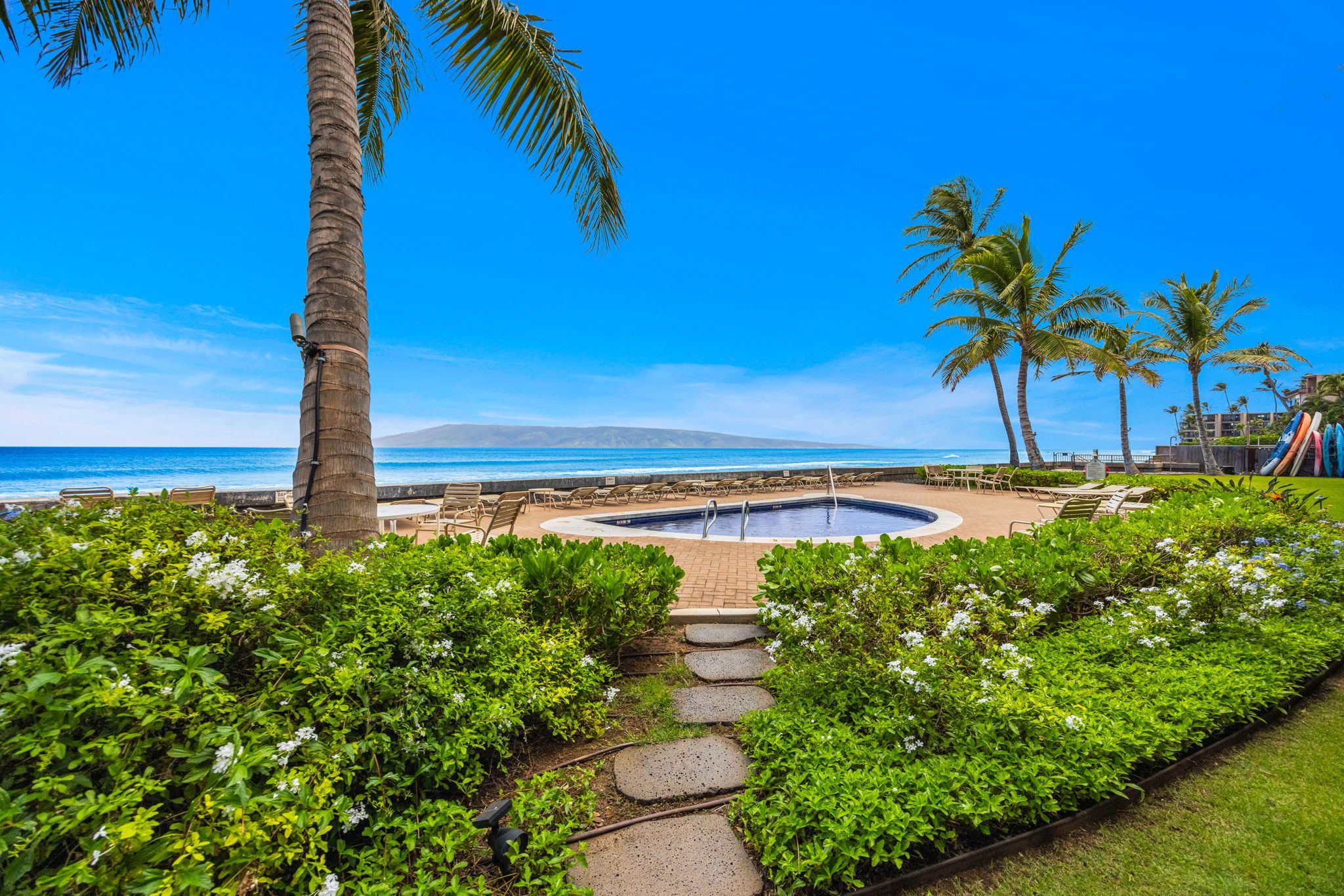 A pool area with lounge chairs and a view of the ocean.
