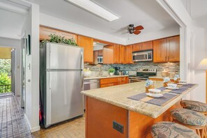 A modern kitchen with wooden cabinets, stainless steel appliances, and a central island with seating. - Remodeled 3BD w AC Pool Near Sandy Beach - Koa Resort 3J (Kihei)