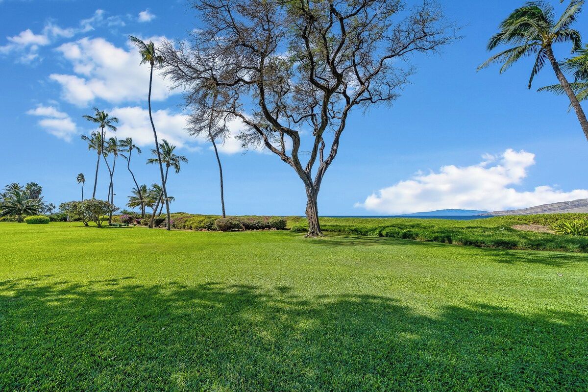 Un paysage verdoyant avec un arbre imposant et des palmiers en arrière-plan.