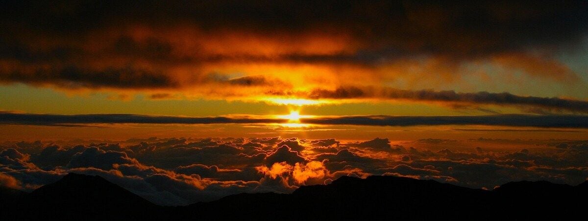 Un atardecer sobre una cadena montañosa con nubes abajo.