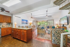 A spacious living area with a sofa, a dining table, and a kitchen with wooden cabinets. - Remodeled 3BD w AC Pool Near Sandy Beach - Koa Resort 3J (Kihei)