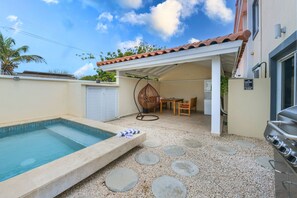 Un patio trasero con piscina, un área de terraza cubierta y una parrilla para barbacoa.