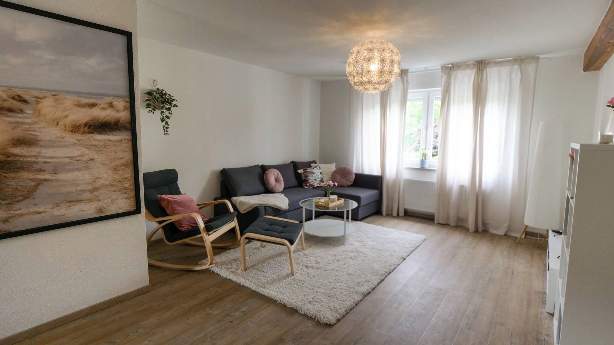 A living room with a sofa, chairs, a coffee table, a hanging plant, and a painting on the wall.