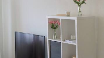 Eine weiße Unterhaltungseinrichtung mit einem Flachbildfernseher, Regalen und dekorativen Elementen, darunter eine Vase mit Blumen.